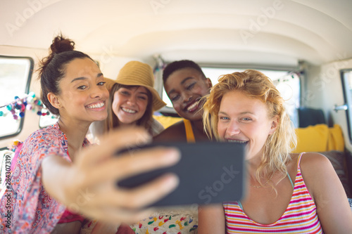 Group of female friends taking selfie with mobile phone in a camper van at beach