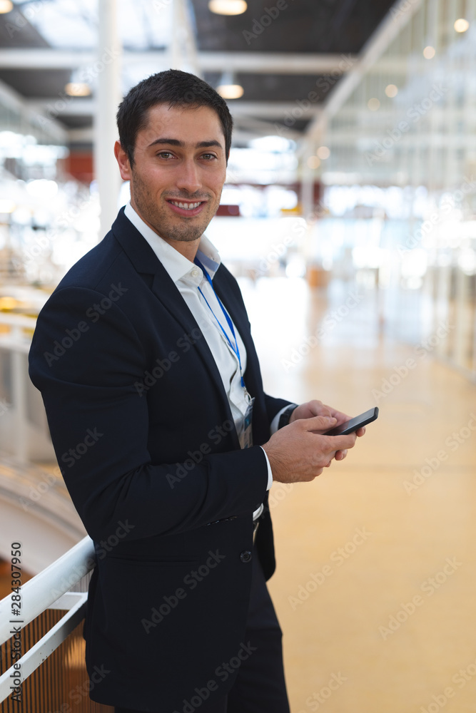 Businessman looking at camera while working on mobile phone in a modern office Businessman looking at camera while working on mobile phone in a modern office