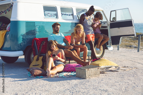 Group of friends using mobile phone near camper van at beach