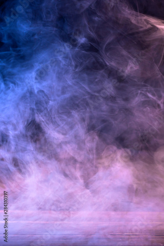 Conceptual image of multi-colored smoke isolated on dark black background and wooden table.