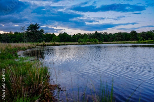 Dramatic sunset reflected in the water of a pond or lake in a countryside landscape