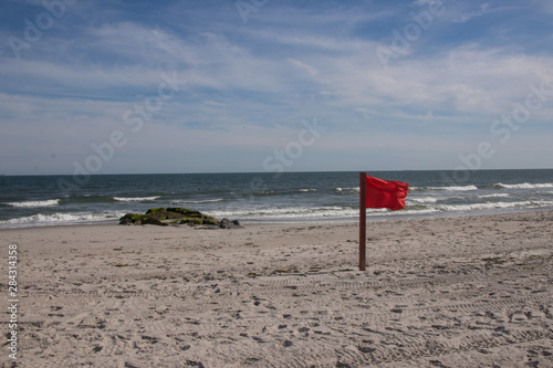 Warning sign of a red flag at a beautiful beach with a blue sky , Long Beach, New York, USA