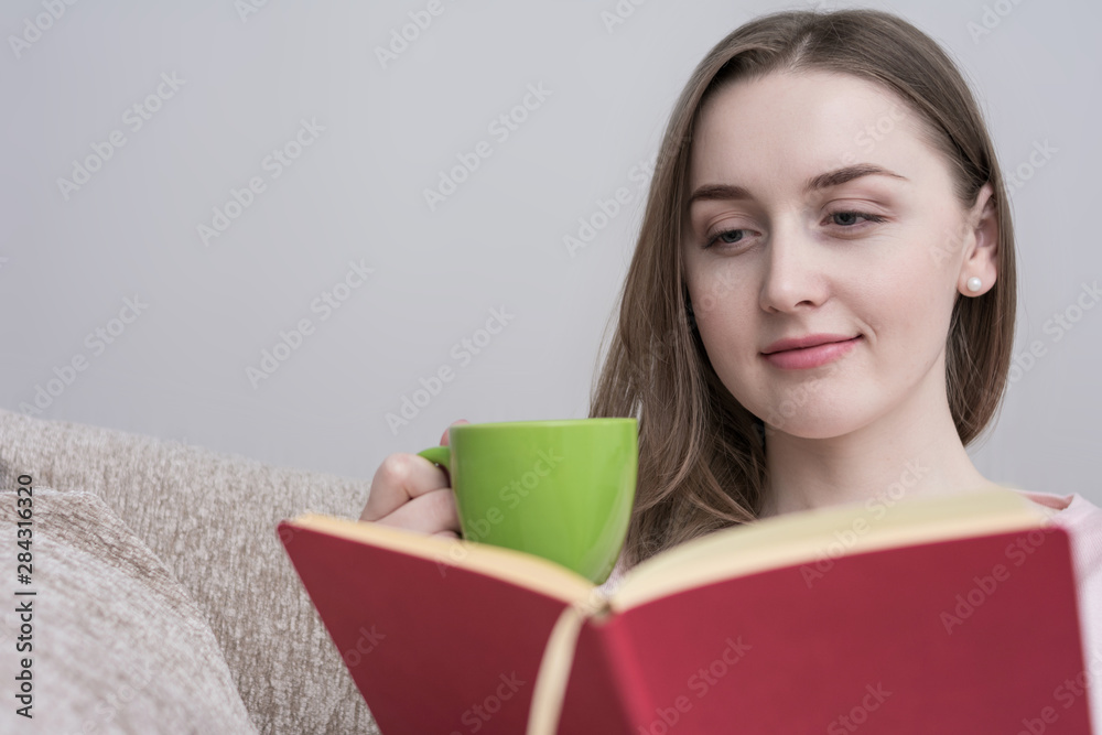 Beautiful woman reading a book, sitting at home on the couch, resting and drinking coffee, close up Beautiful woman reading a book, sitting at home on the couch, resting and drinking coffee, close up
