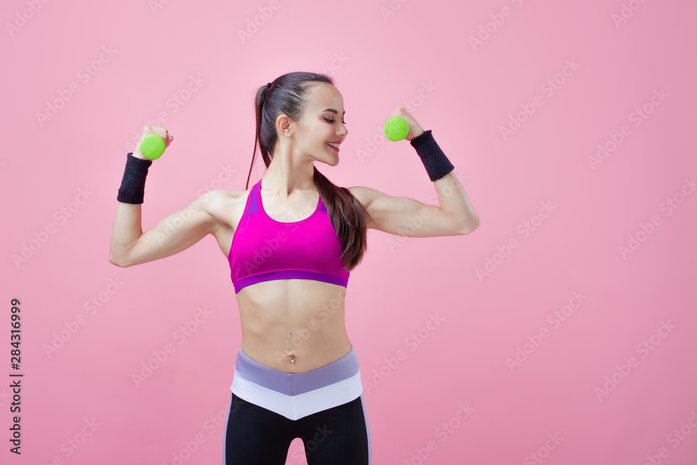 A young athletic attractive brunette girl with a ponytail shows off her biceps, holding dumbell in hand. Girl power. A young athletic attractive brunette girl with a ponytail shows off her biceps, holding dumbell in hand. Girl power.