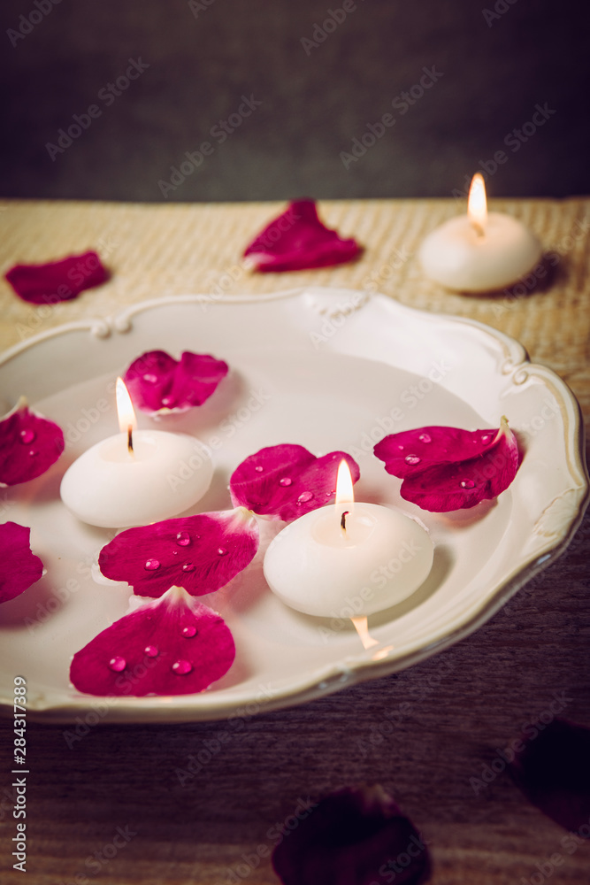 Rose hip( Rosa rugosa, beach rose, Japanese rose) petals floating in water with spa candles, beauty rose water concept. Rose hip( Rosa rugosa, beach rose, Japanese rose) petals floating in water with spa candles, beauty rose water concept.