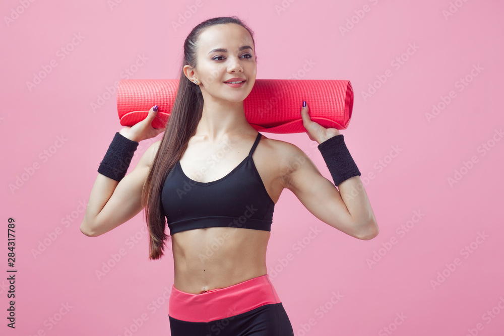 A brunette girl, attractive, is standing, holding a yoga mat over the shoulders. A brunette girl, attractive, is standing, holding a yoga mat over the shoulders.
