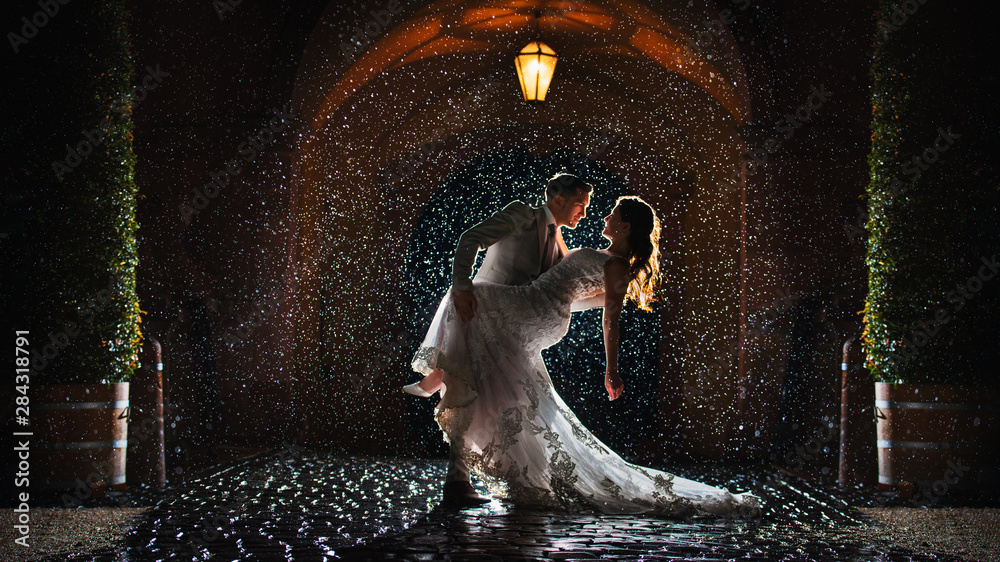 a bride and groom is dancing happily in the rain - obrazy, fototapety, plakaty 
