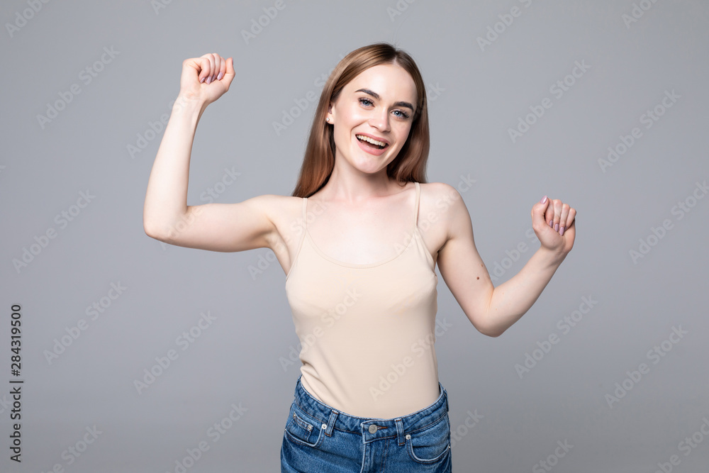 Used to success. Happy young woman in casual wear gesturing and keeping eyes closed while standing against grey background Used to success. Happy young woman in casual wear gesturing and keeping eyes closed while standing against grey background