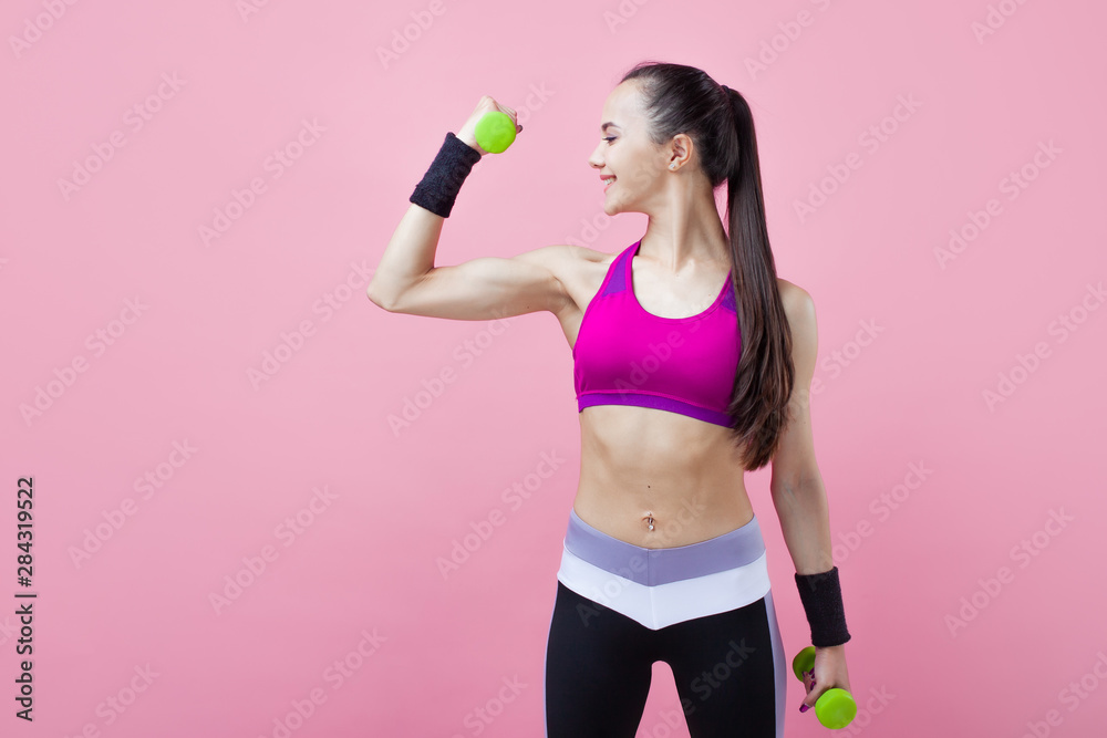A young athletic attractive brunette girl with a ponytail shows off her biceps, holding dumbell in hand. Girl power. A young athletic attractive brunette girl with a ponytail shows off her biceps, holding dumbell in hand. Girl power.