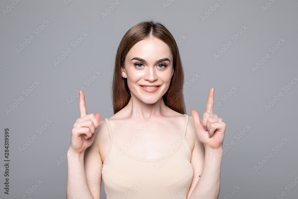 Pretty young brunette woman gesturing up with fingers on gray background Pretty young brunette woman gesturing up with fingers on gray background