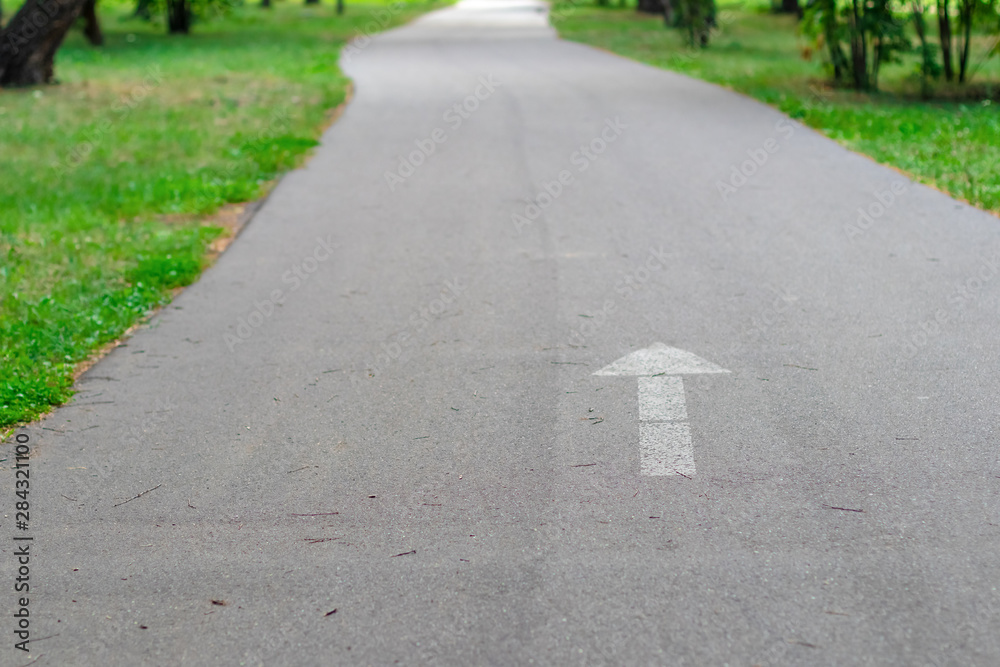 Obraz premium Bicycle or jogging sports track with copy space. Sign the direction of movement of white paint on asphalt, selective focus.