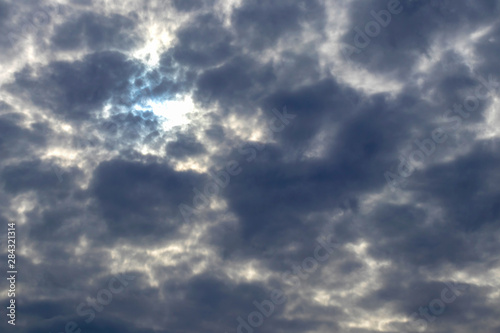 Through dense dark clouds, a bright sun breaks through without visible rays, a natural background.