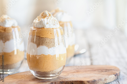 Homemade pumpkin trifle dessert made from pumpkin puree, cream cheese, cookie crumbs and whipped cream. Extreme selective focus with blurred background. photo