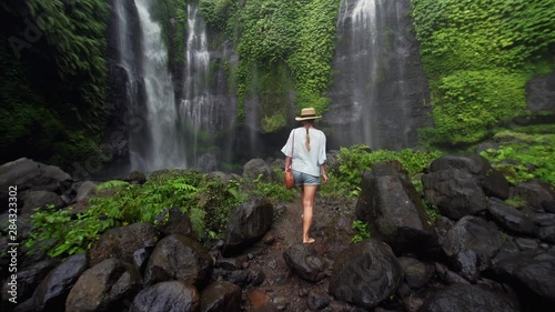 Wallpaper Mural Barefooted woman in shorts and straw hat is walking through small pond on wet rocks and enjoying incredible waterfall Sekumpul (95m) in Bali Rainforest. Indonesia Torontodigital.ca