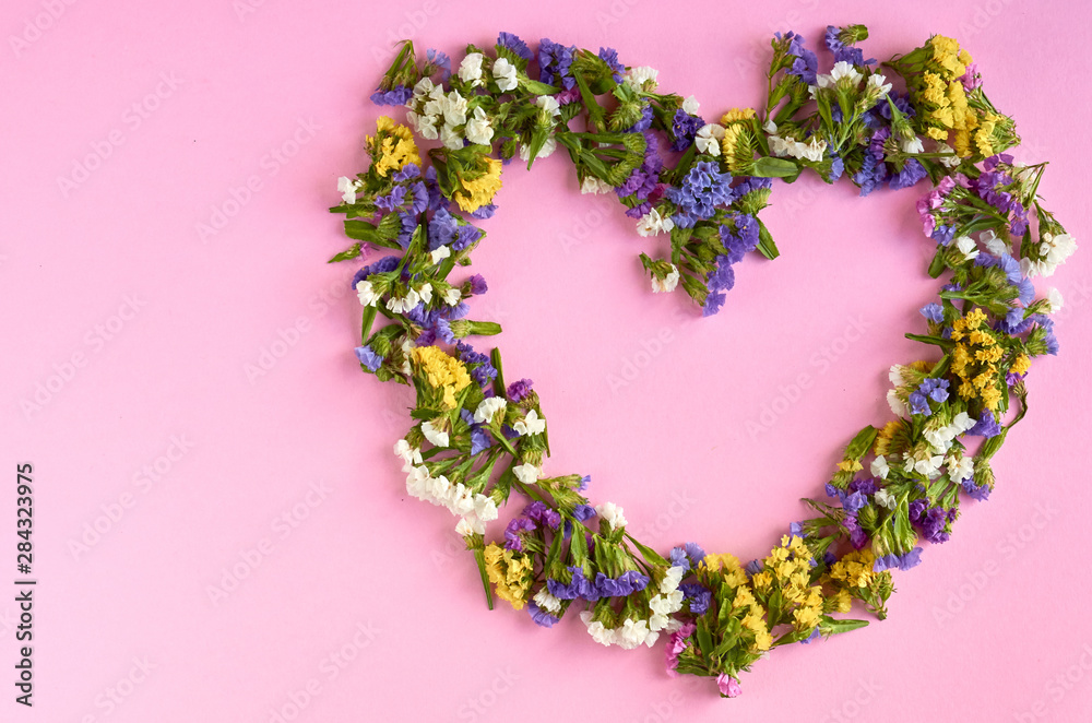 Colored flowers on pink background composition, heart shape.