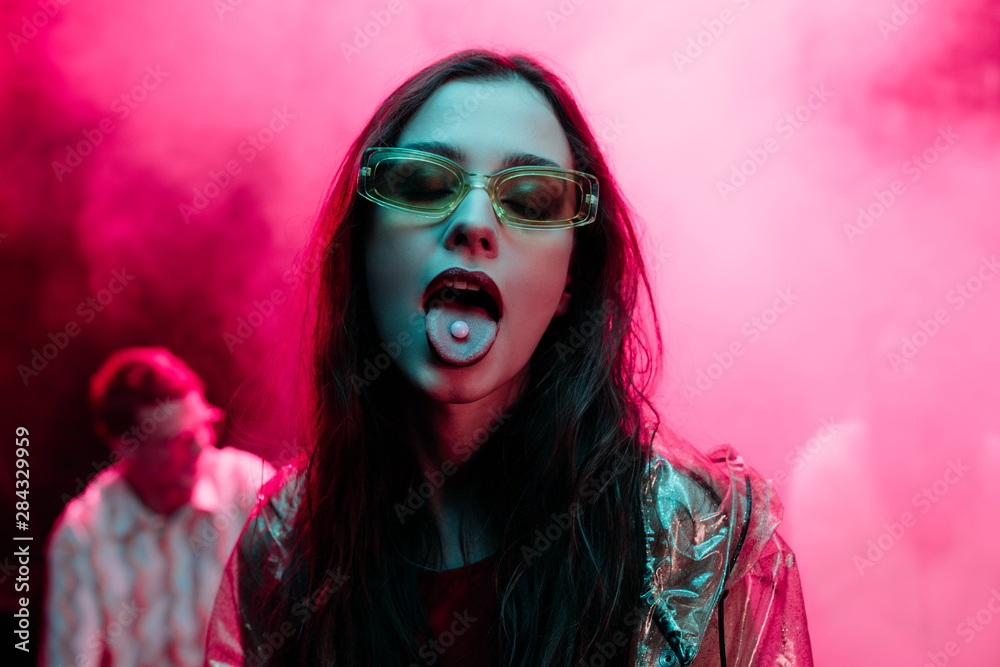 beautiful girl in sunglasses with lsd on tongue in nightclub with pink  smoke Stock-foto | Adobe Stock