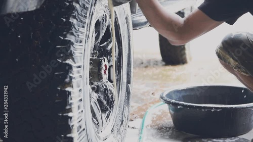 Car wash staff are using a sponge moistened with soap and water to clean the wheels of the car.