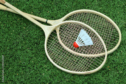Badminton shuttlecock and racket on green grass of stadium, top view.