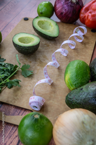 Halved avocado guacamole ingredients on wooden cutting board with measuring tape