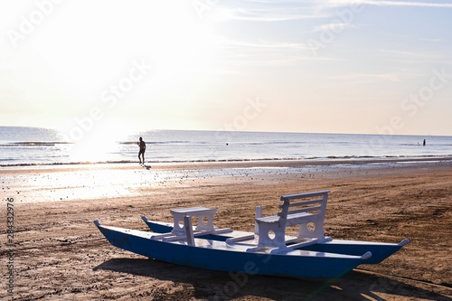 Catamaran with a white wooden seat by the sea. Sandy beach and sunny dawn. Beautiful horizon and sun flare.