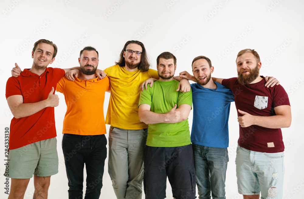 Young men weared in LGBT flag colors isolated on white background. Caucasian male models in shirts of red, orange, yellow, green, blue and purple. LGBT pride, human rights, choice concept. Look happy. Young men weared in LGBT flag colors isolated on white background. Caucasian male models in shirts of red, orange, yellow, green, blue and purple. LGBT pride, human rights, choice concept. Look happy.