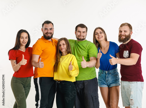 Young man and woman weared in LGBT flag colors on white background. Caucasian models in bright shirts. Look happy, smiling and hugging. LGBT pride, human rights and choice concept.