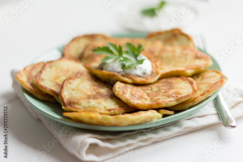 fresh delicious zucchini pancakes with sour cream and herbs on the table
