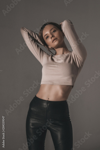 Attractive sexy fashion woman with brunette hairstyle in reglan and leather pants. Portrait of seductive hot stylish woman model on white background in studio