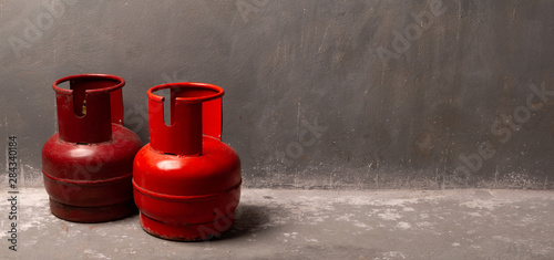 Two old red gas cylinders are standing on the floor near the wall. photo