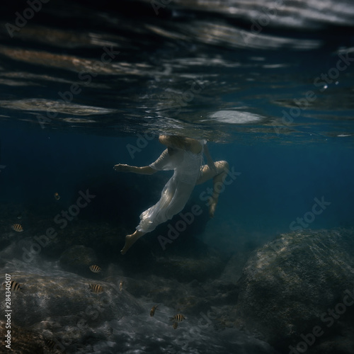 Woman in white swims underwater in the sea