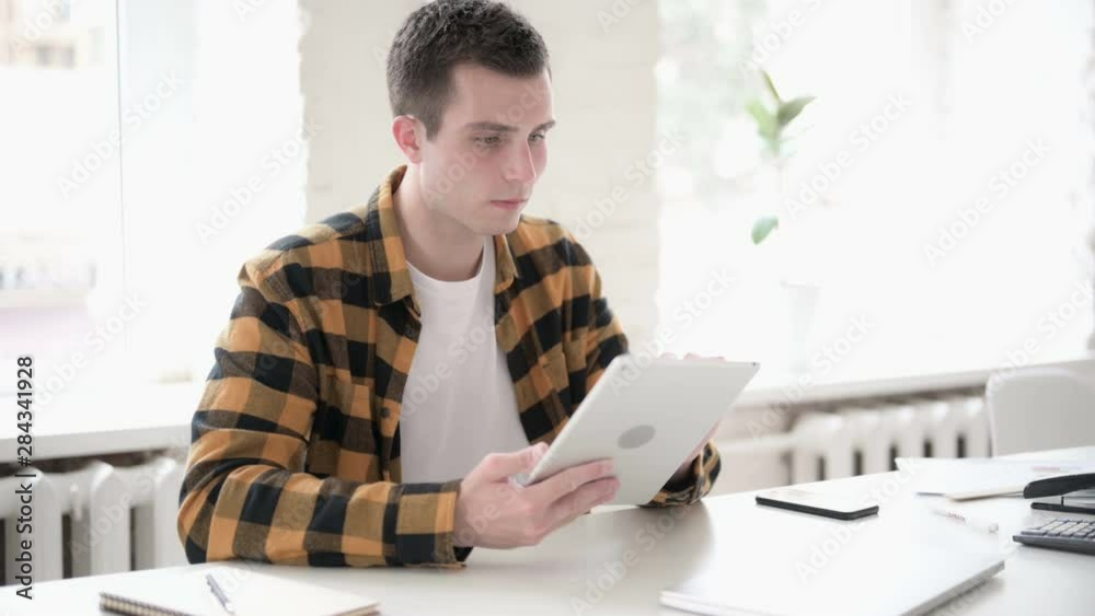 Casual Young Man Scrolling Internet on Tablet Casual Young Man Scrolling Internet on Tablet