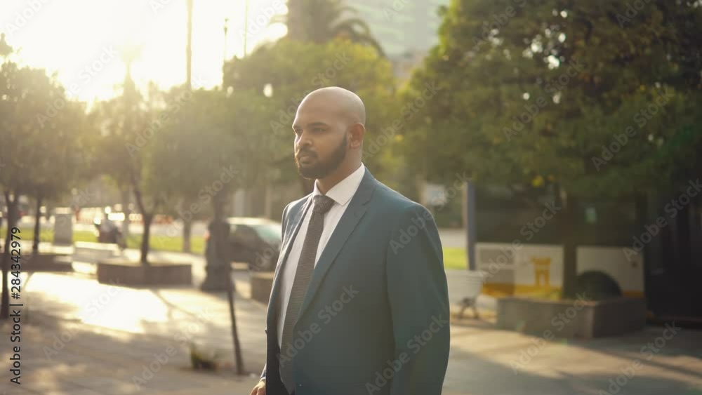 Indian businessman wearing blue suit standing with travel bag or suitcase near office or hotel. Travel business concept Indian businessman wearing blue suit standing with travel bag or suitcase near office or hotel. Travel business concept