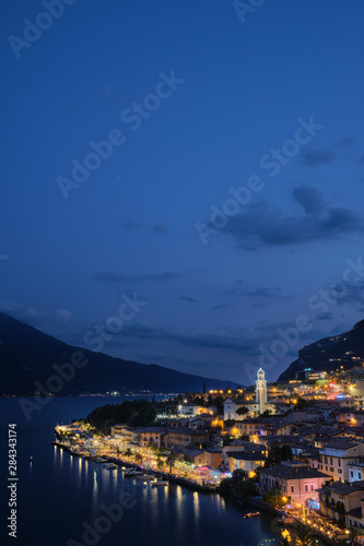 Panoramic view of night city Limone Sul Garda region Trento Lake Garda Italy. A popular resort town. Summer time of the year. Aerial view. City night lanterns, reflection of lamps.