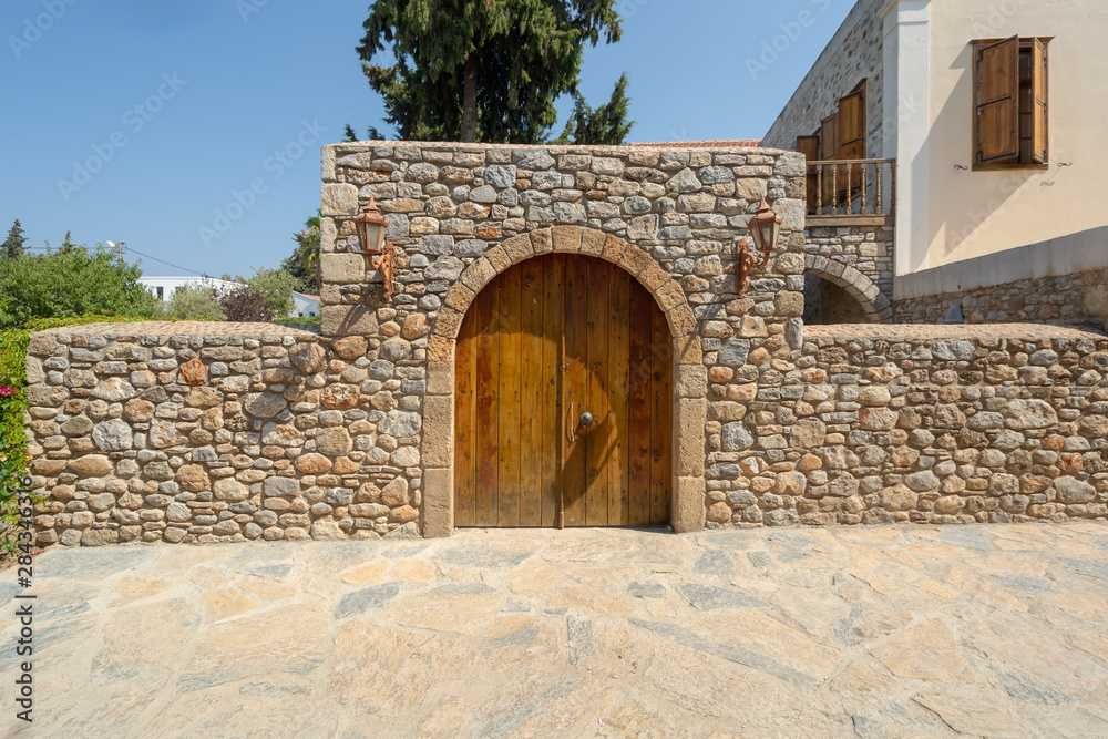 Old varnished wooden door and stone wall with lanterns on both sides. Old Mediterranean style of Datca, Turkey.