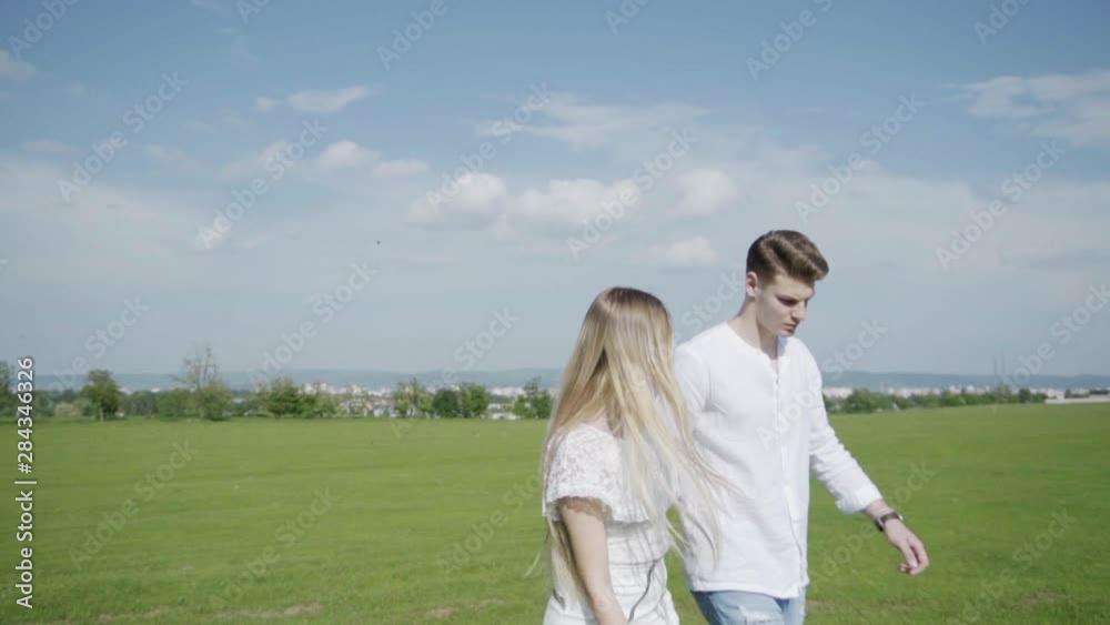 Just Married Couple In Casual Clothes Walking Through Green Field, Slow Motion Just Married Couple In Casual Clothes Walking Through Green Field, Slow Motion
