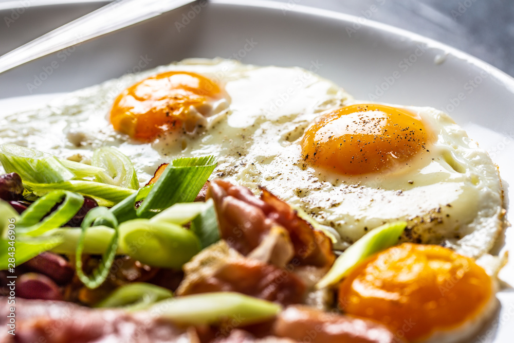 English Breakfast with eggs, bacon, beans and iyoung onion in white plate English Breakfast with eggs, bacon, beans and iyoung onion in white plate