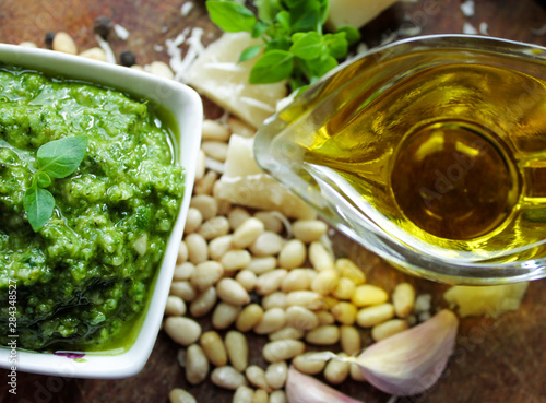 Close-up of a bowl with pesto sauce and some ingredients for its preparation: green Basil, Parmesan cheese, pine nuts, salt and garlic on the background of aged boards