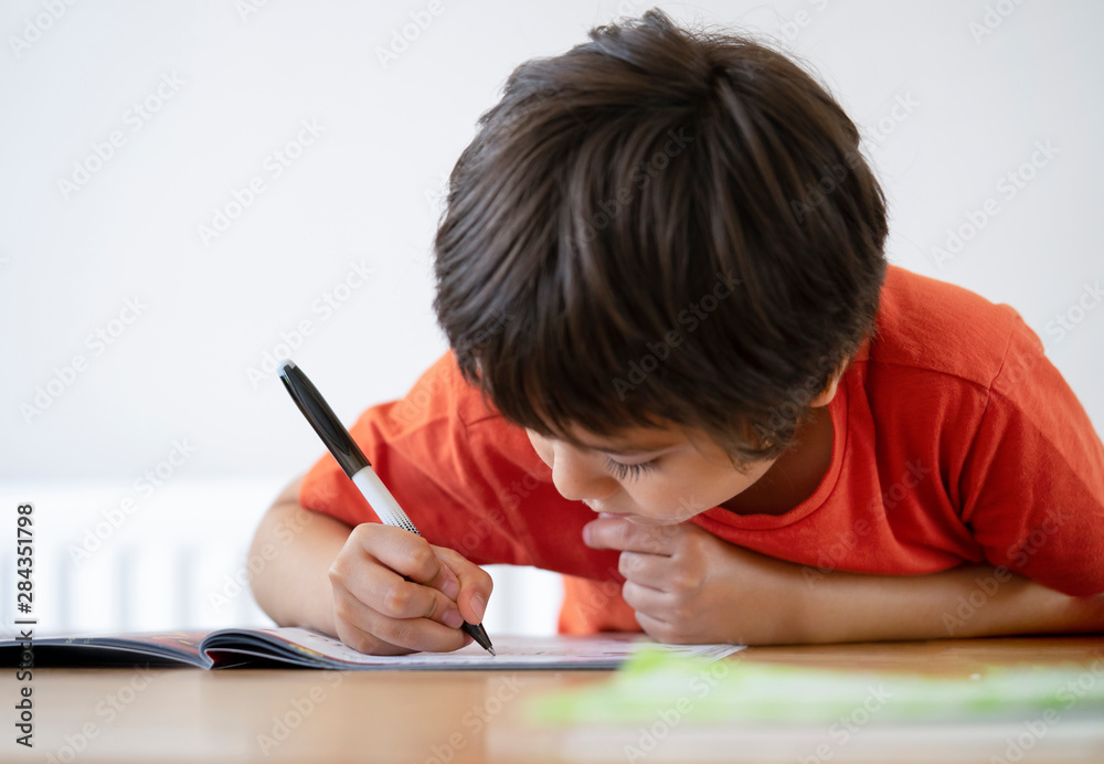 School kid boy siting on table doing homework with white background, Happy Child holding black pen,Little boy is writing on white paper at the table,Elementary school and education concept School kid boy siting on table doing homework with white background, Happy Child holding black pen,Little boy is writing on white paper at the table,Elementary school and education concept