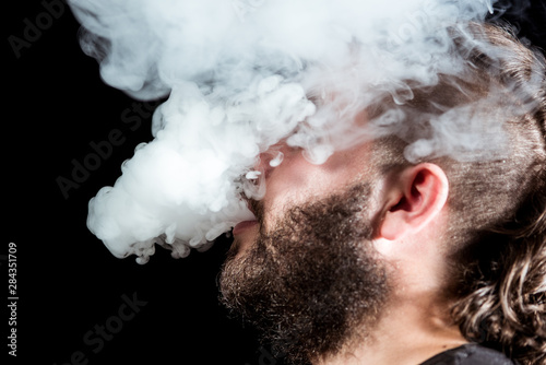 Man with a leafy beard exhales smoke through his mouth and surrounds him on black background