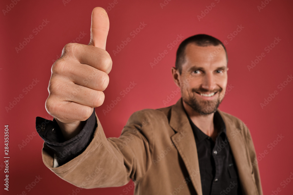 Middle-aged man with beard and mustache, wears black shirt and brown jacket posing against a red background. Sincere emotions concept. Middle-aged man with beard and mustache, wears black shirt and brown jacket posing against a red background. Sincere emotions concept.
