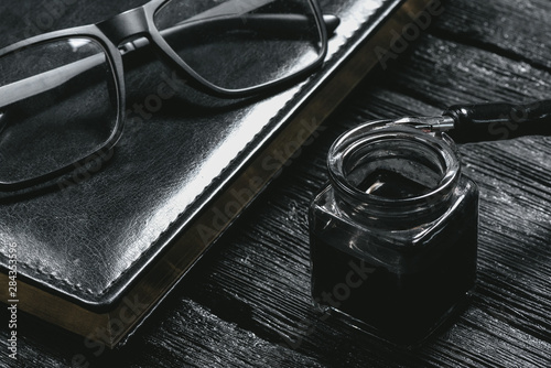 Business book, inkwell with a quill pen and eye glasses on black wooden table. Business concept background.