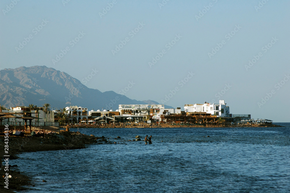 EGYPT, Dahab. Houses, and palm trees of a small city built on the shore of the red sea, at the foot of a pink mountain 