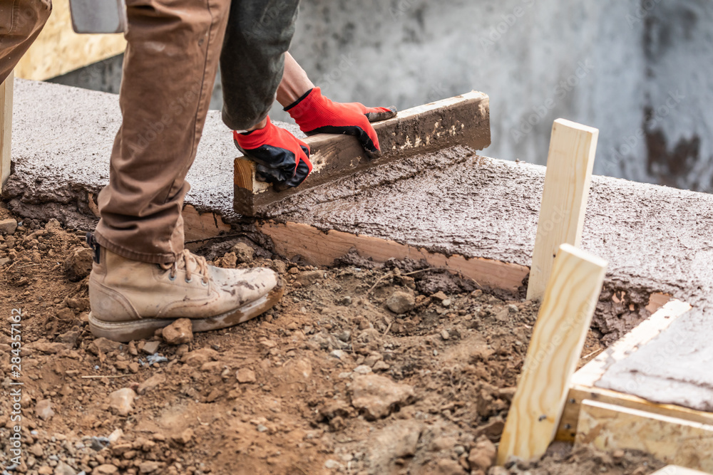 Construction Worker Leveling Wet Cement Into Wood Framing Construction Worker Leveling Wet Cement Into Wood Framing