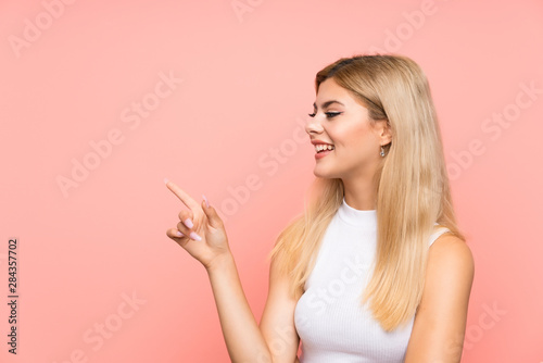 Teenager girl over isolated pink background pointing finger to the side