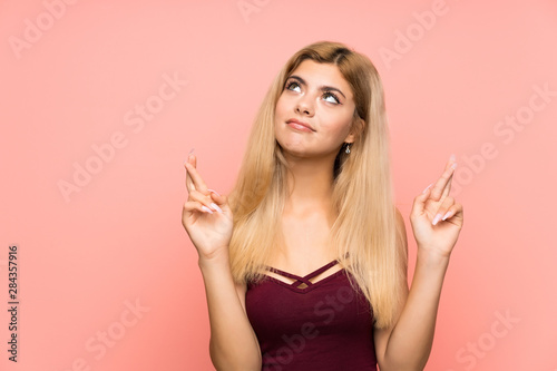 Teenager girl over isolated pink background with fingers crossing