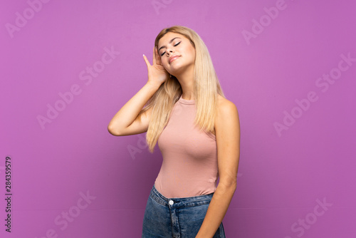 Teenager girl over isolated purple background listening to something by putting hand on the ear