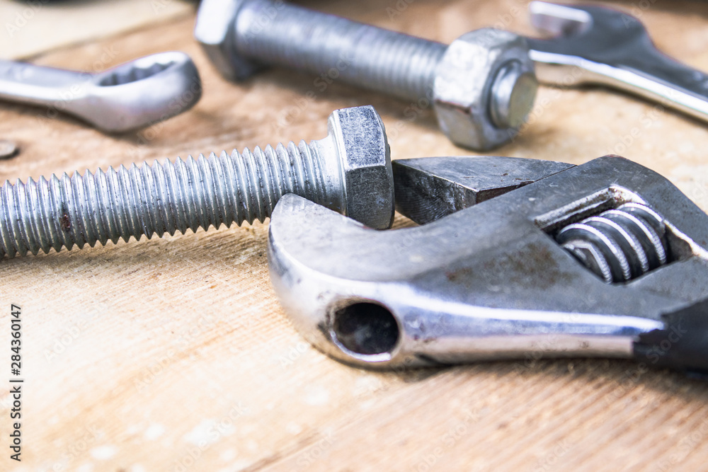 An adjustable spanner lies near the bolts and nuts of the washer against the background of wooden boards. An adjustable spanner lies near the bolts and nuts of the washer against the background of wooden boards.