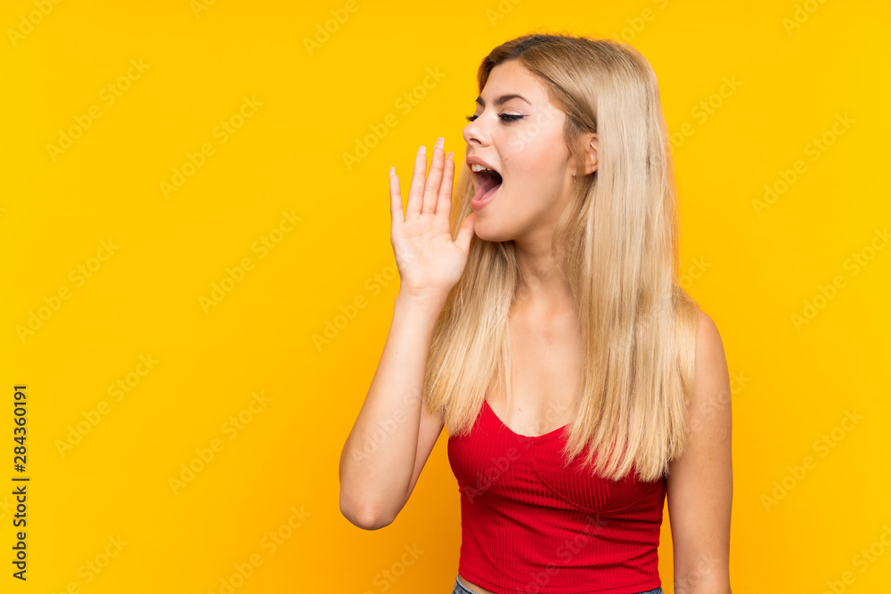 Teenager girl over isolated yellow background shouting with mouth wide open Teenager girl over isolated yellow background shouting with mouth wide open
