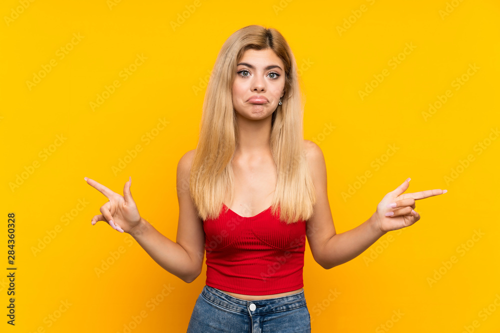 Teenager girl over isolated yellow background pointing to the laterals having doubts Teenager girl over isolated yellow background pointing to the laterals having doubts