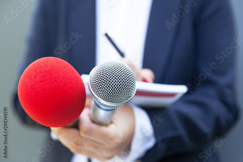 Female journalist at news conference or media event, writing notes, holding microphone